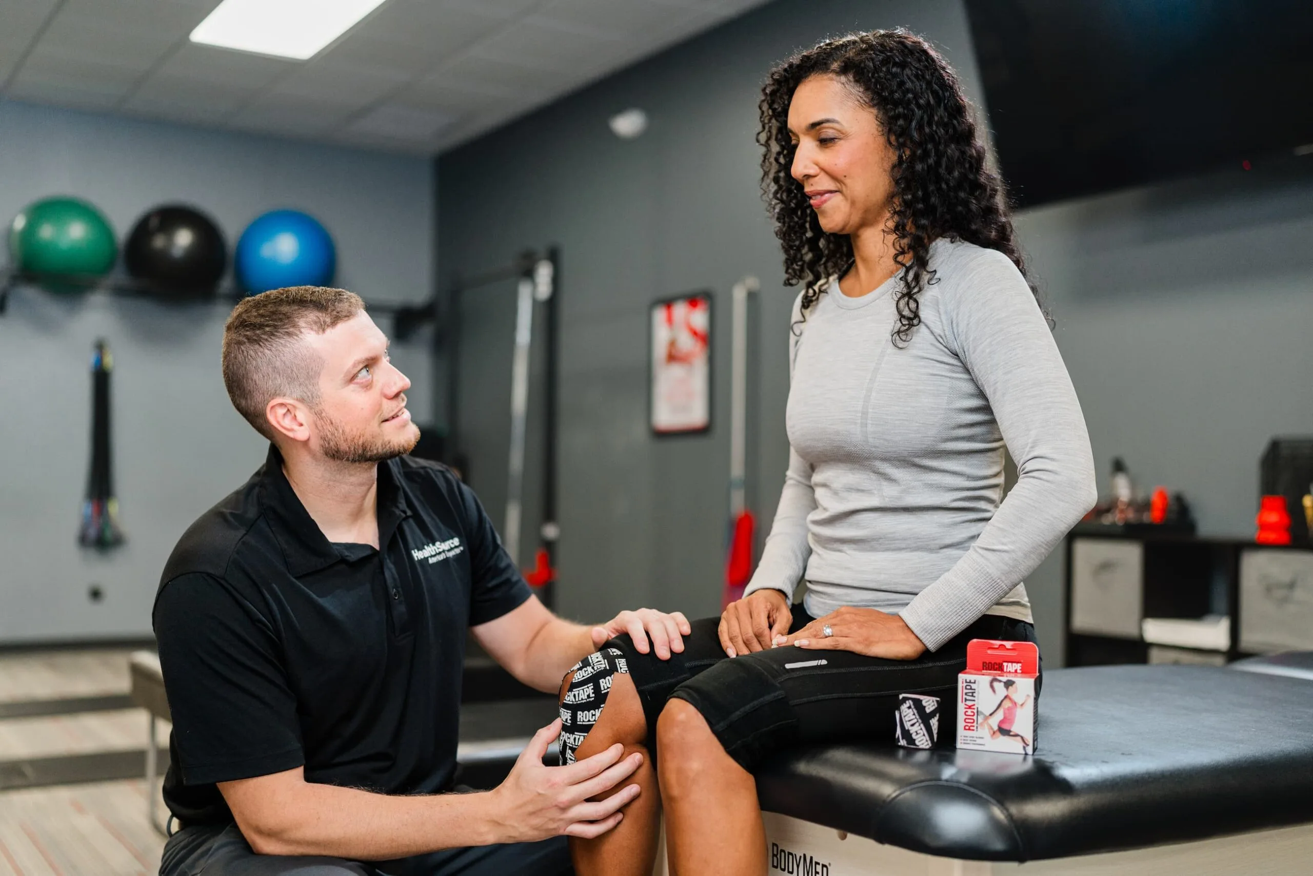 Practitioner checks with patient as they place tape on her knee.