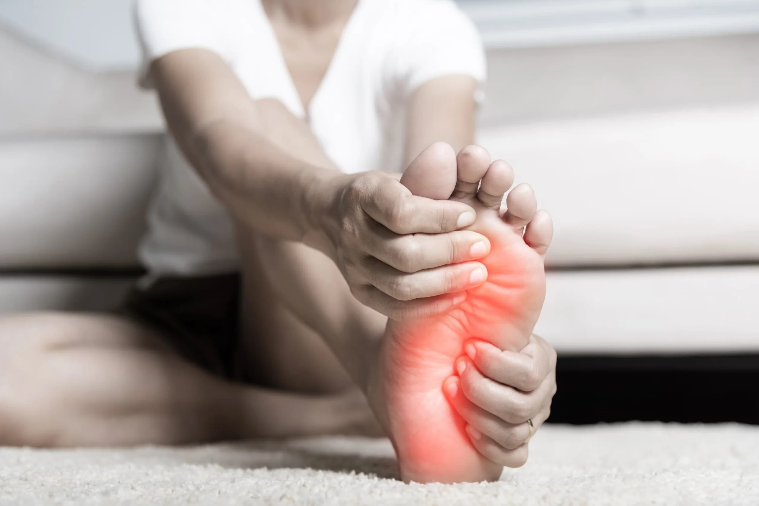 Close up of a person's foot, highlighted in red, with their hands wrapped around and gripping in pain.