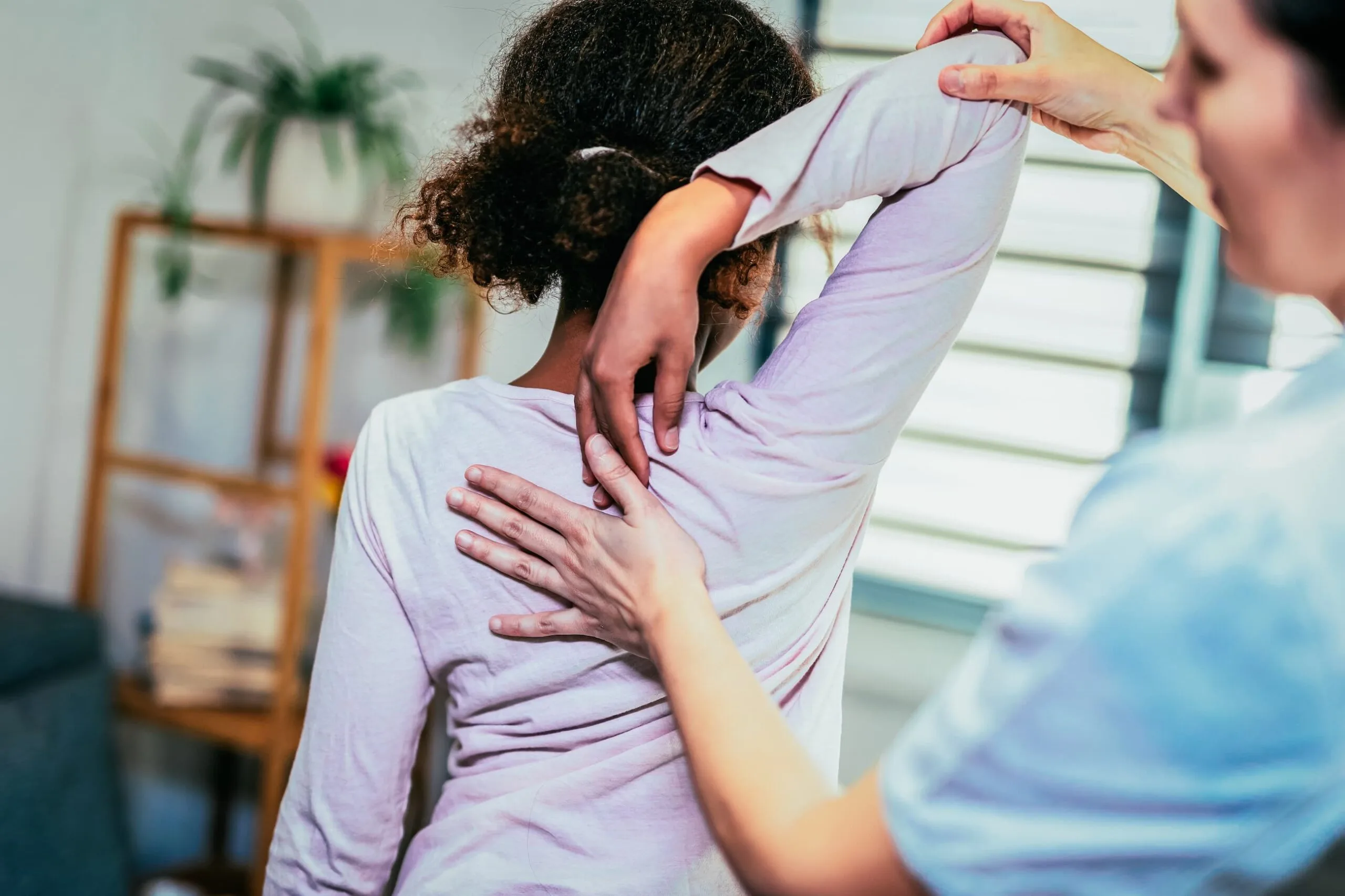 Young child in medical office points between their shoulder blades as a practitioner examines.