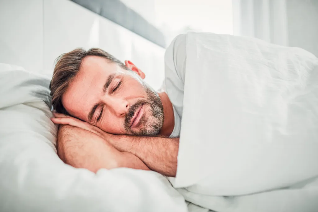 Middle-aged man sleeping in bed, looking peaceful.
