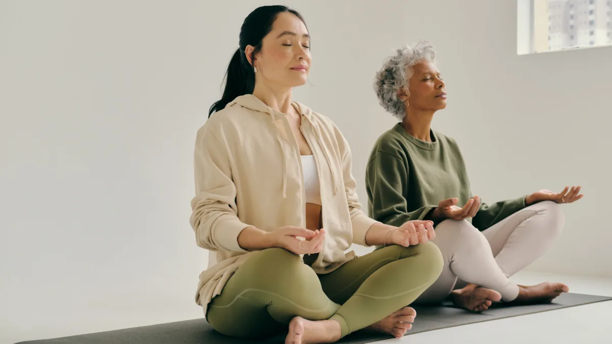 Two women sharing a yoga mat while practicing yoga on the floor