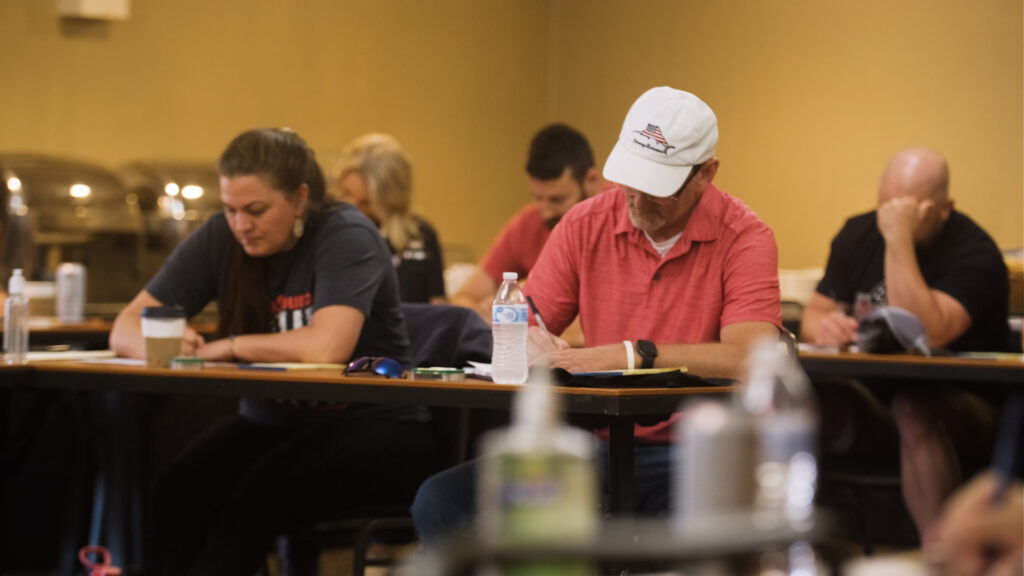 Team members sit at tables, writing notes during a team training event.