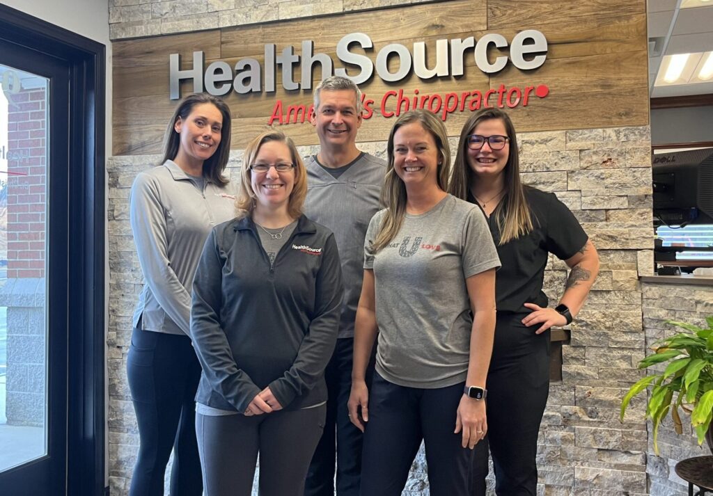 Franchise team take group photo in front of HealthSource wall sign.