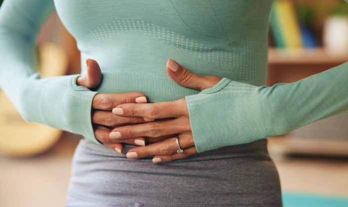 A woman in athletic wear holds her stomach, indicating bloating or digestive discomfort, symbolizing gut health issues.
