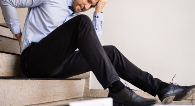 Office worker sitting on stairs holding his lower back in pain after a workplace injury.