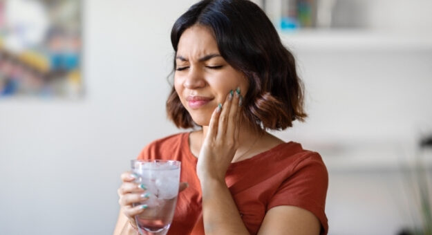 Woman holding a glass of water while touching her jaw, showing discomfort from jaw pain.