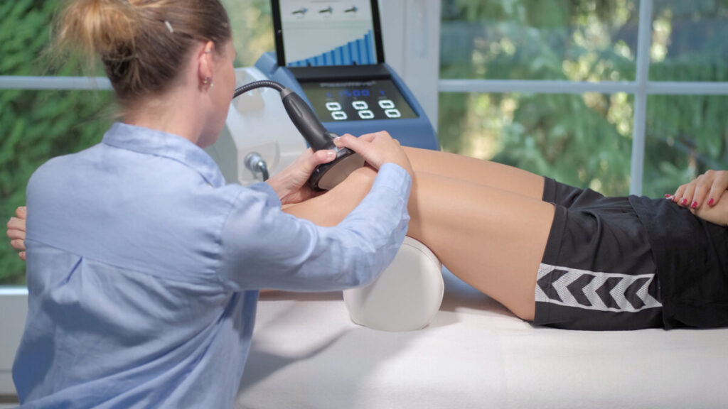 Clinician using shockwave therapy device on patient’s leg in treatment setting
