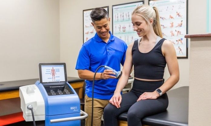 Chiropractor performing shockwave therapy on a patient’s arm in a clinical setting to treat pain and promote healing
