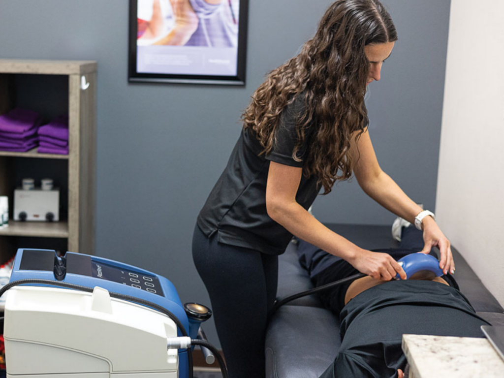 A clinician performs shockwave therapy on a patient’s back while on an exam table in a chiropractic office. This non-invasive treatment is used to reduce pain, support tissue healing, and improve mobility for musculoskeletal conditions.