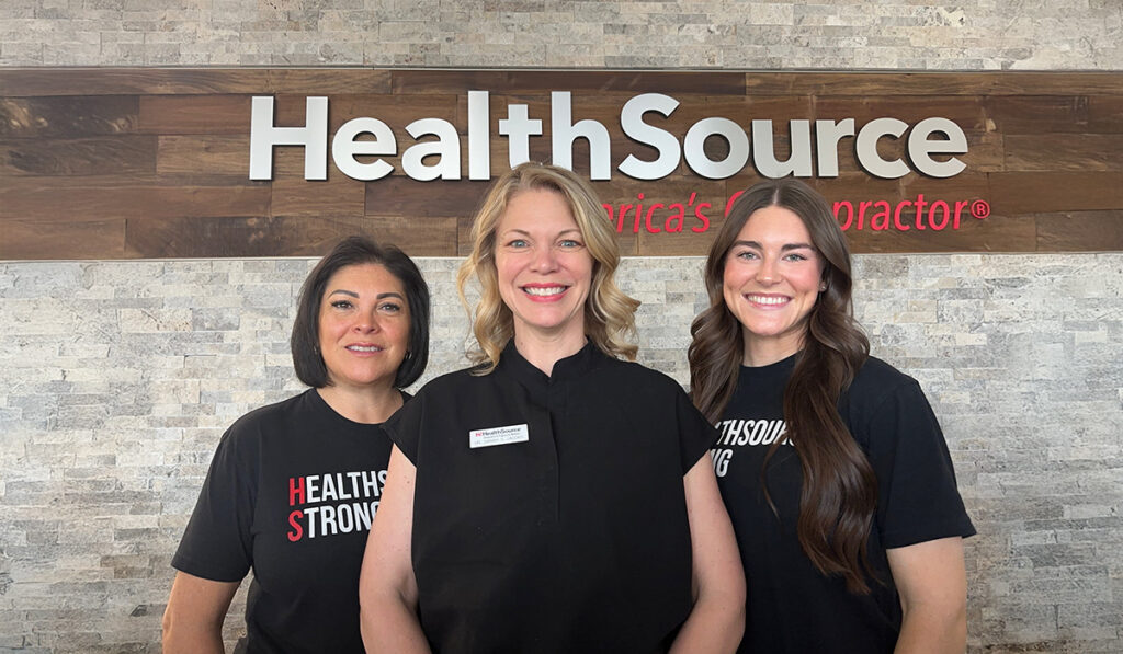 Dr. Sarah Jacobs, Doctor of Chiropractic, and the team at HealthSource of Huntsville - Merchants Walk, posing together near the front desk of the clinic.