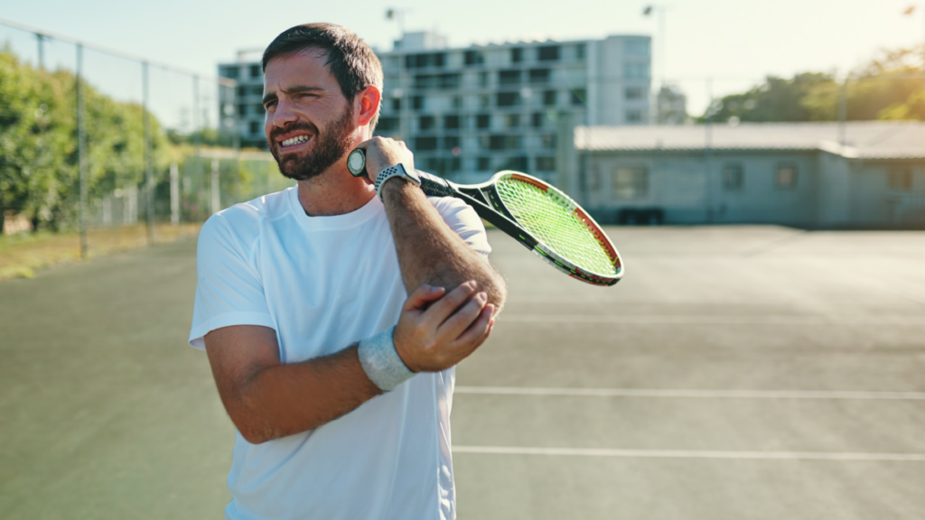 Man experiencing elbow pain while playing tennis, showing symptoms of tennis elbow, a common repetitive strain injury treated with chiropractic care and rehabilitation.