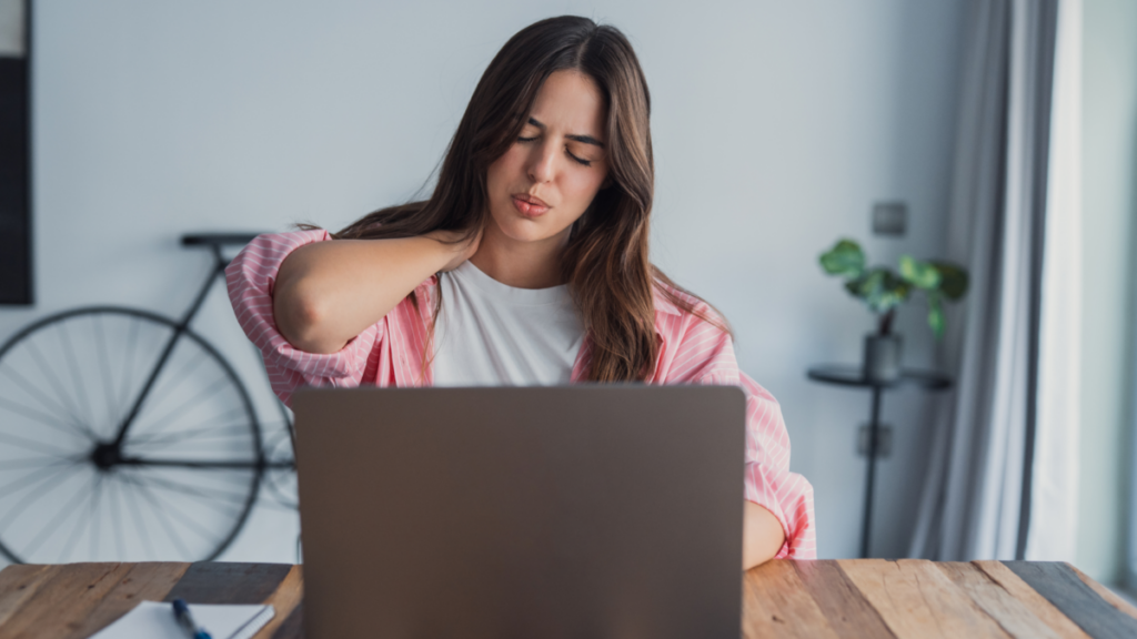 Woman experiencing neck pain while working at a laptop, demonstrating a repetitive stress injury commonly associated with desk work, screen time, and poor ergonomics.