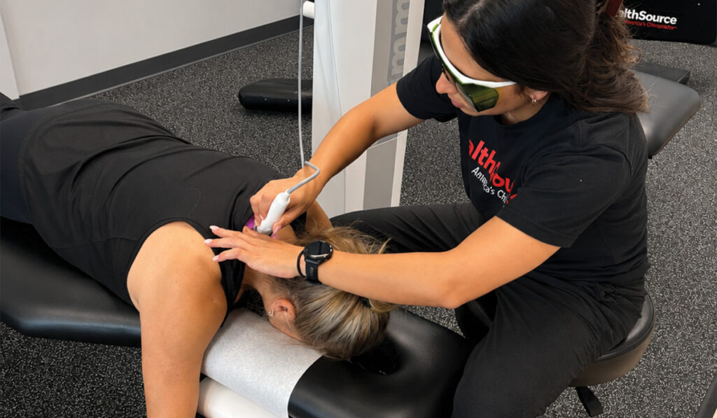A patient receiving Class IV laser treatment on upper shoulder and back of neck area at a HealthSource clinic.